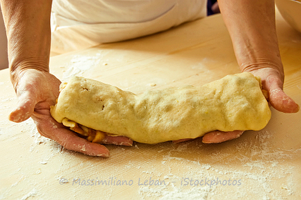 Someone is holding an apple strudel that is ready to go in the oven