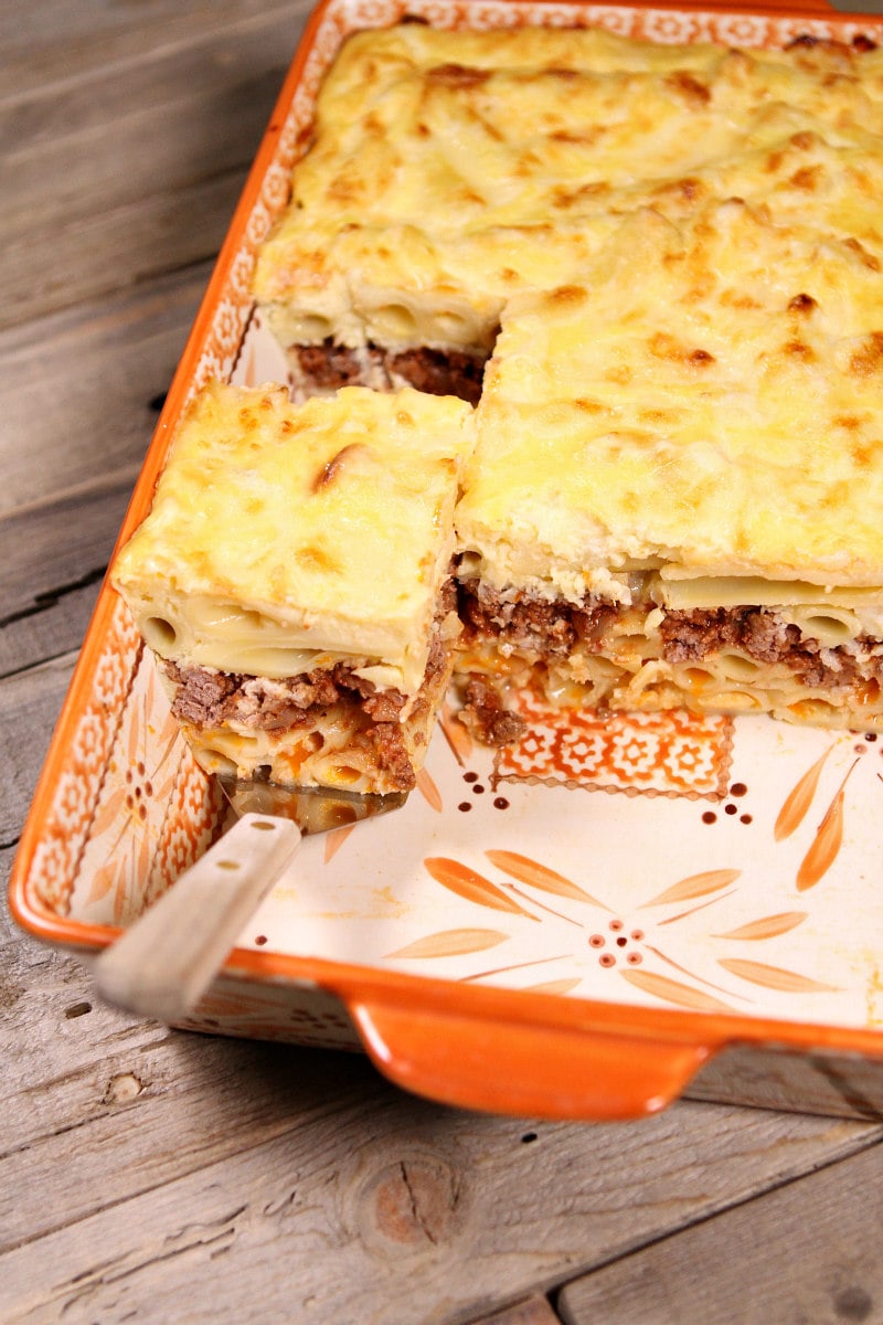 overhead shot of pastitsio in a casserole dish using a spatula to take out a slice
