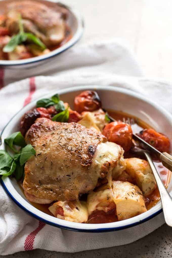 Baked Italian Chicken with Potatoes and cherry tomatoes in a bowl with a knife and fork, ready to be eaten.